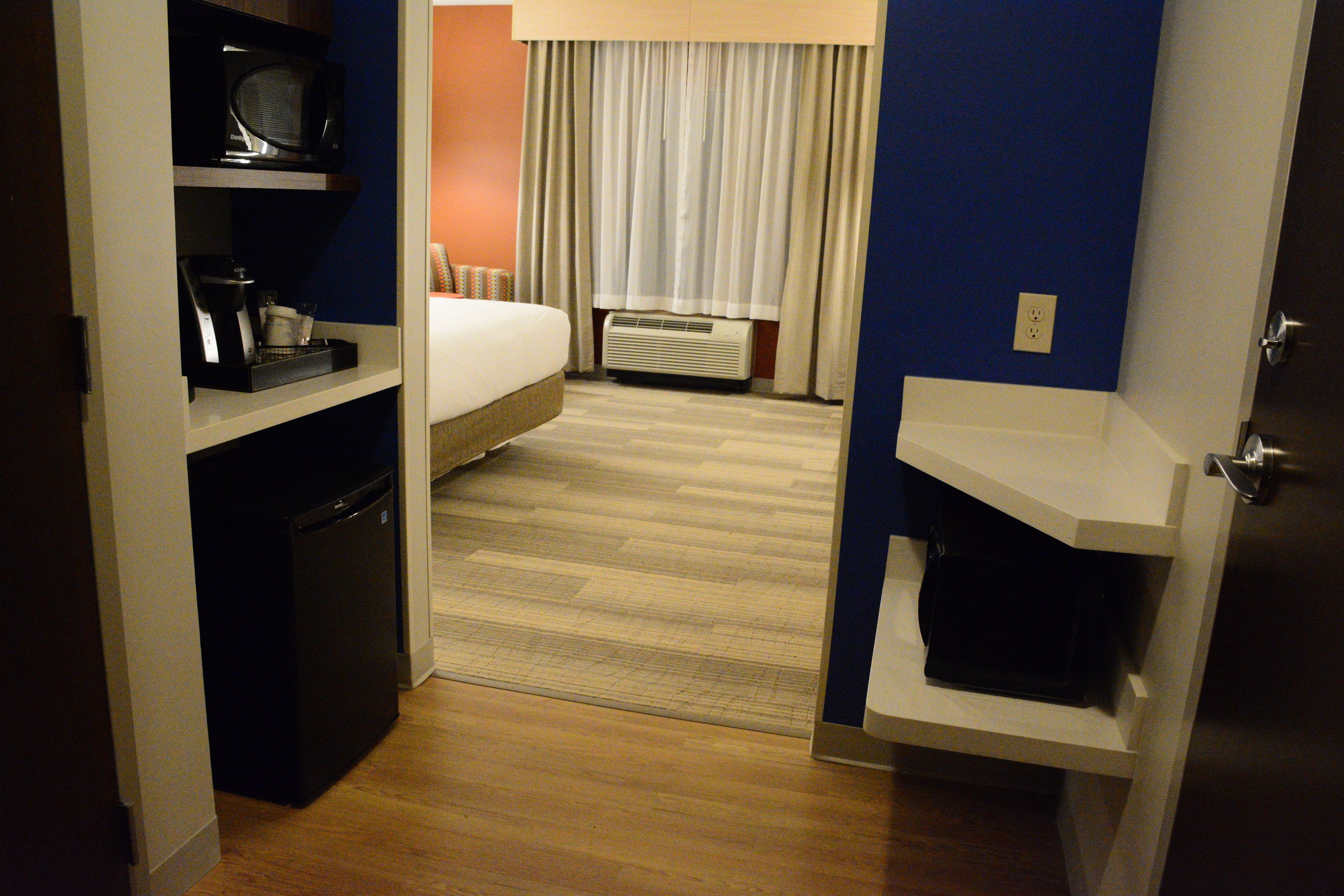 A hotel room with a bed, a microwave, a mini-fridge, and a built-in air conditioner.
