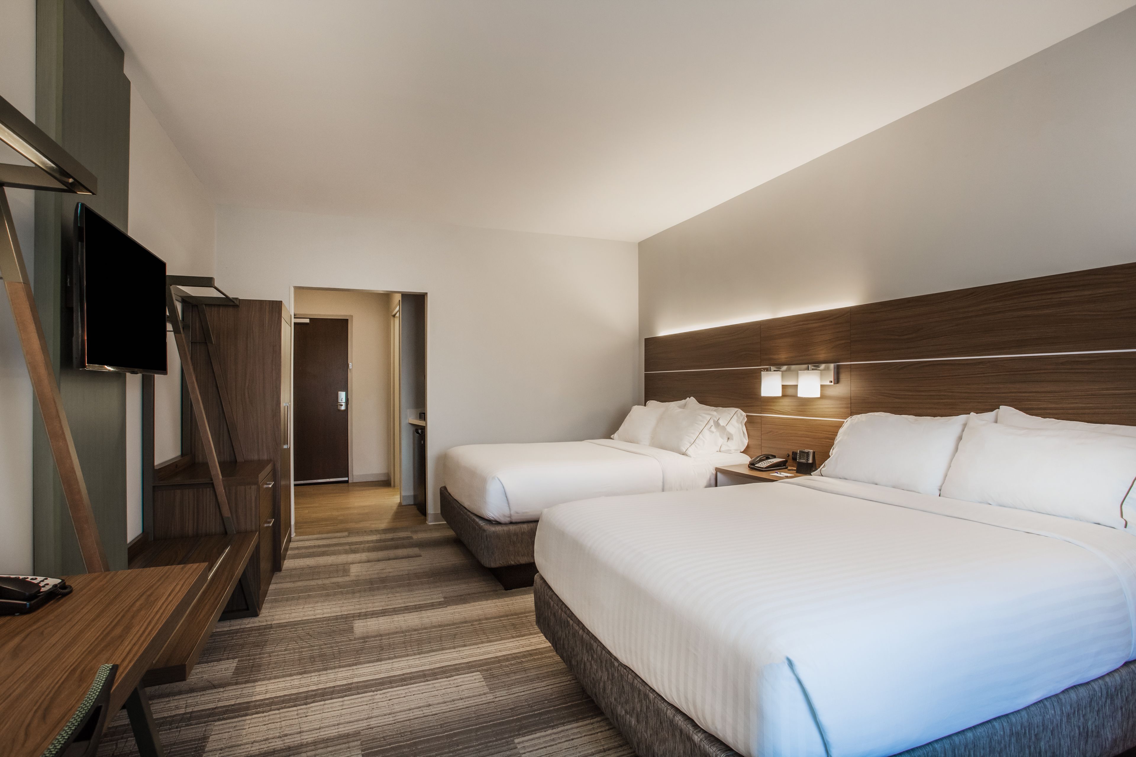 A hotel room with two beds, a desk, a TV, and a wooden headboard.