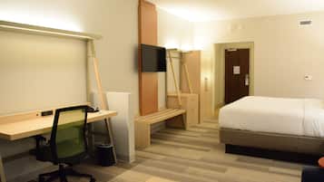 A hotel room with a desk, chair, bed, and a television mounted on the wall.