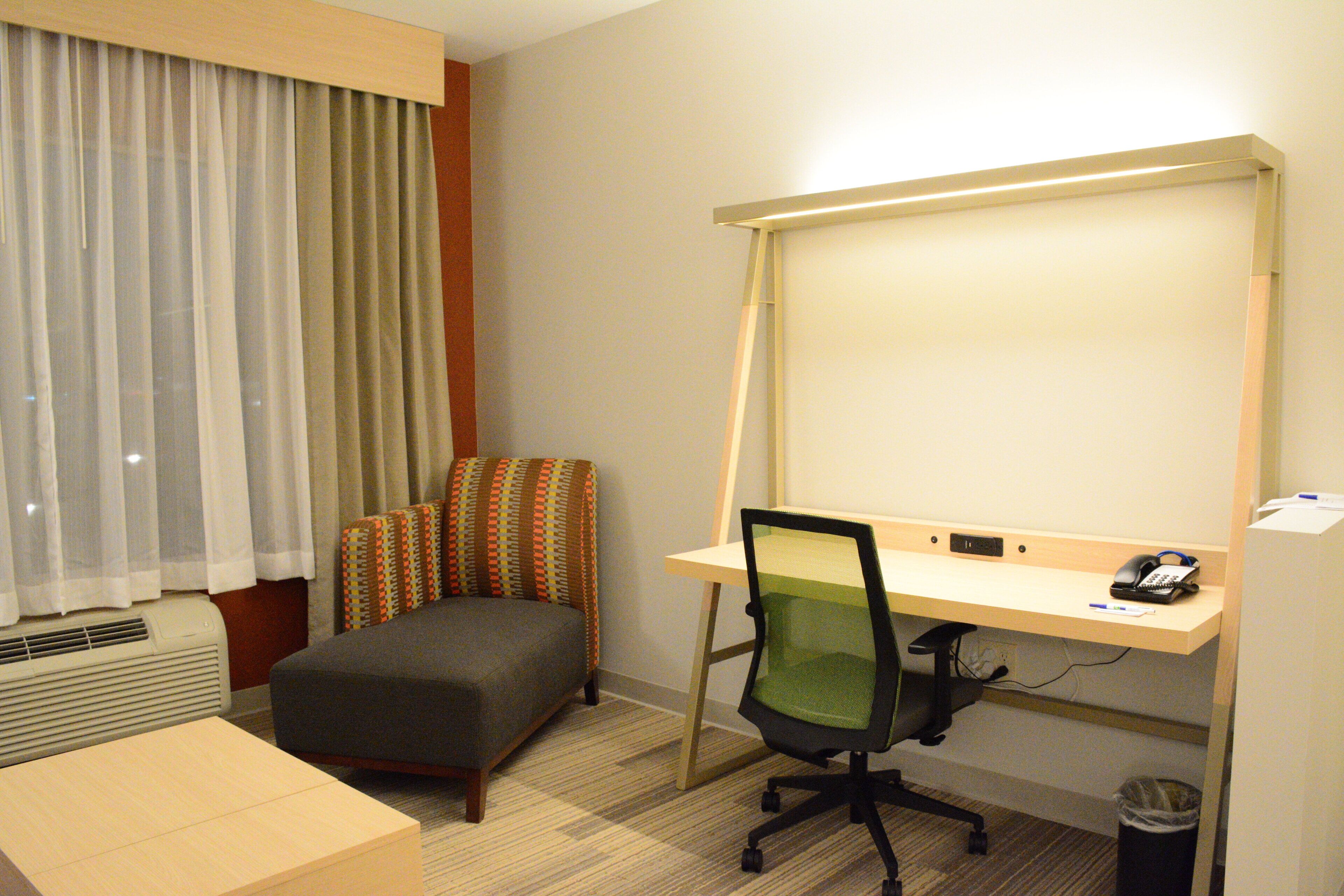 A hotel room with a desk, chair, and a large window with curtains.