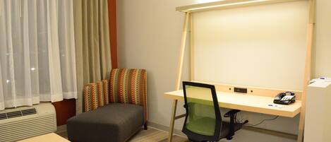 A hotel room with a desk, chair, and a large window with curtains.