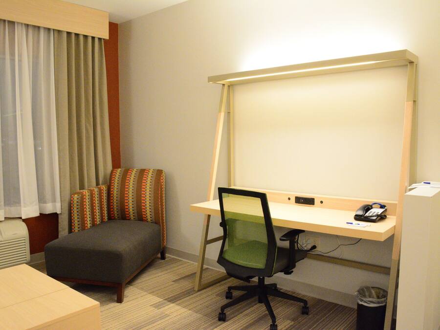 A hotel room with a desk, chair, and a large window with curtains.