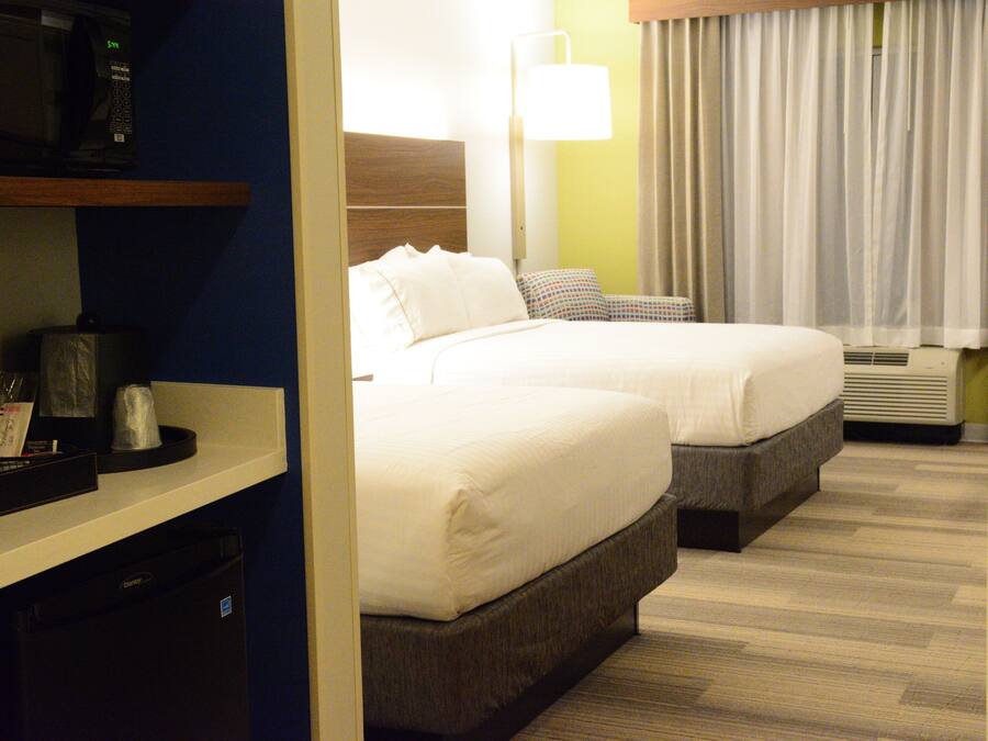 Ein Hotelzimmer mit zwei Betten, einer Mikrowelle, einer Lampe und einem Fenster mit Vorhängen.