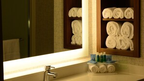 Un baño con un espejo grande, un lavabo y estantes con toallas enrolladas.