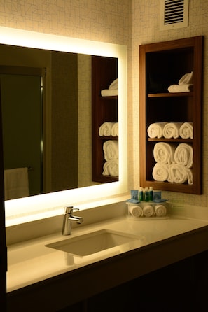 A bathroom with a large mirror, a sink, and shelves with rolled towels.