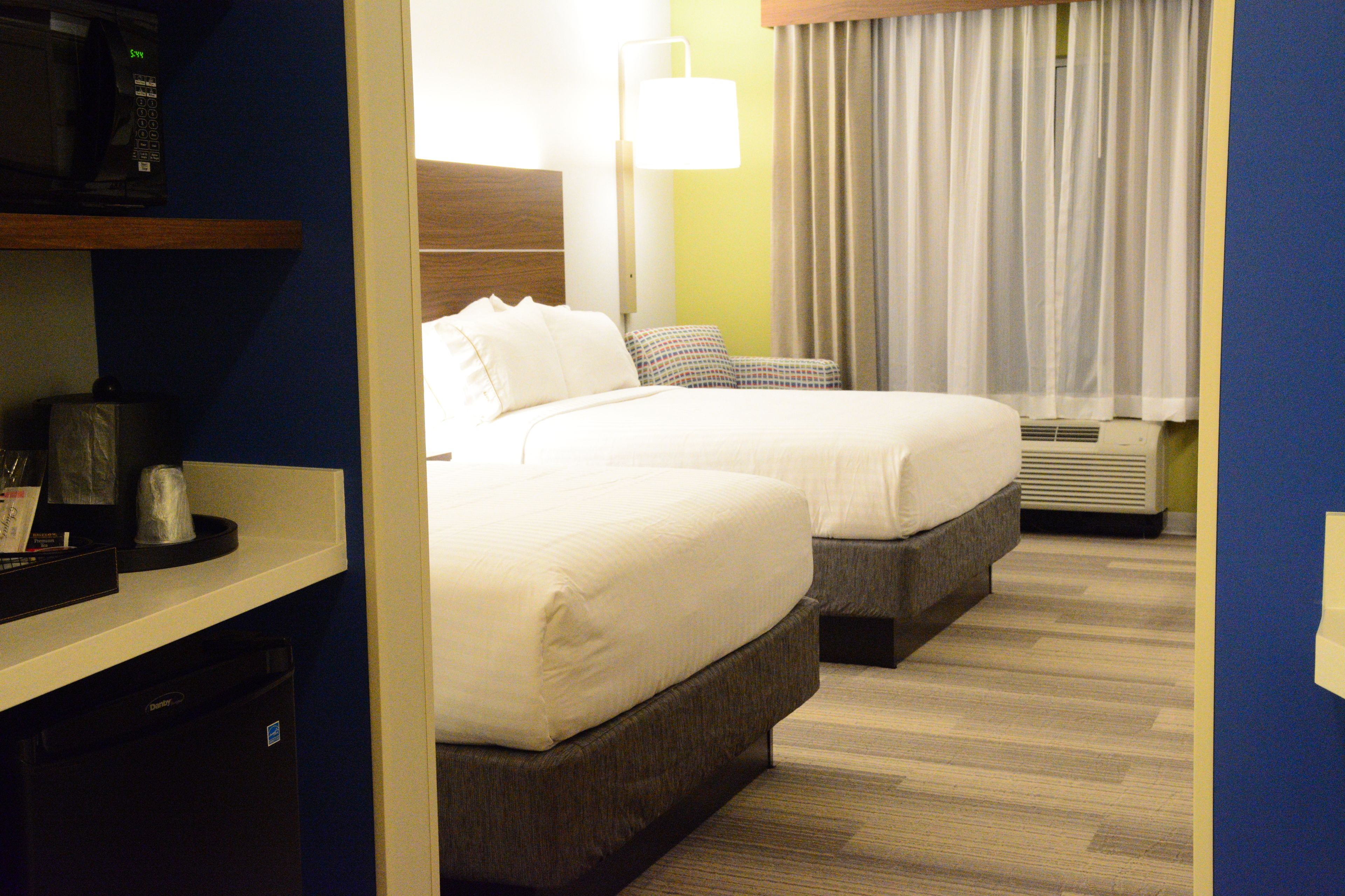 Een hotelkamer met twee bedden, een magnetron, een lamp en een raam met gordijnen.