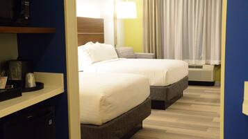 Een hotelkamer met twee bedden, een magnetron, een lamp en een raam met gordijnen.