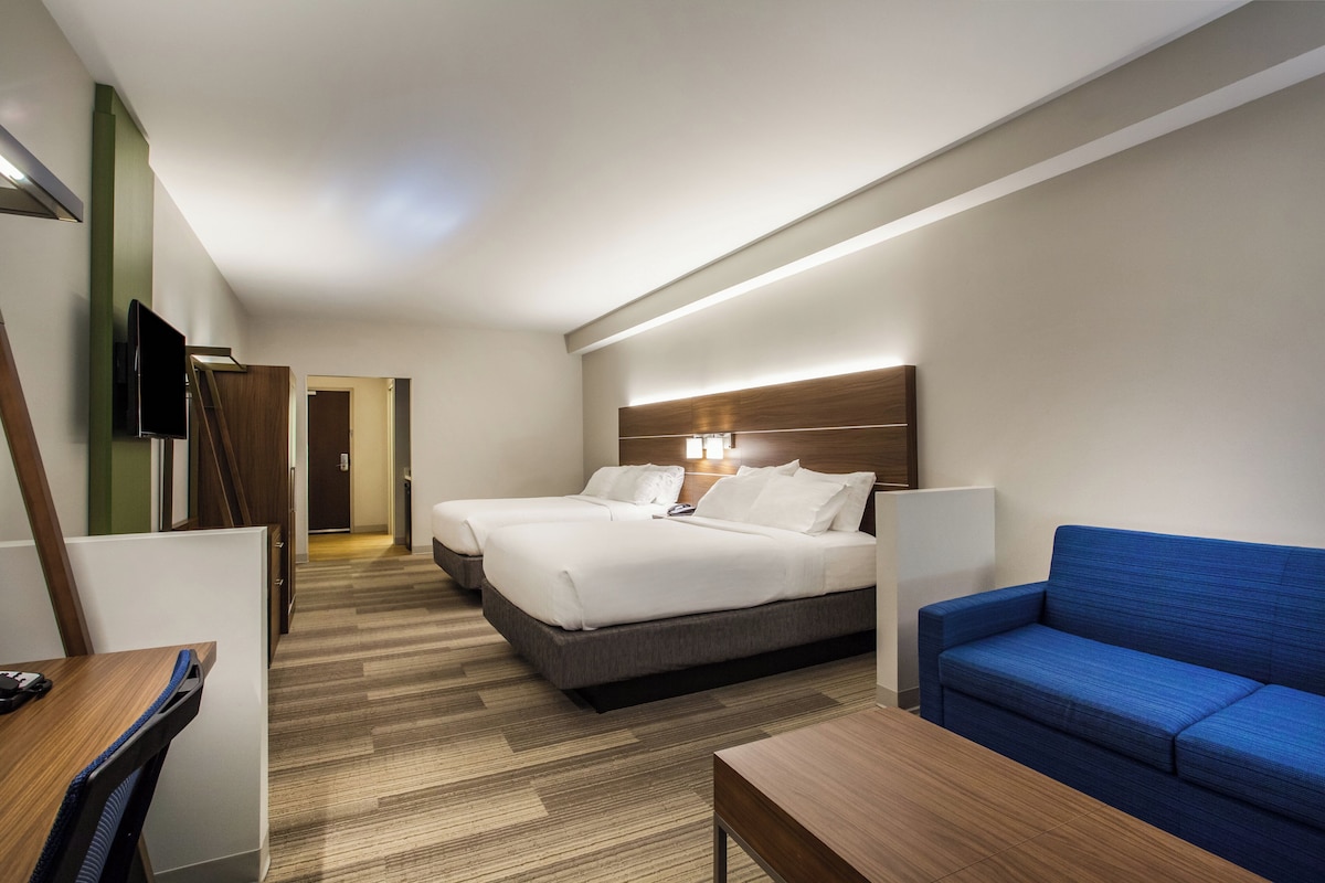 A hotel room with two beds, a blue sofa, a wooden desk, and a TV.