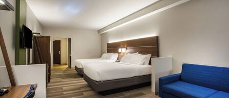 A hotel room with two beds, a blue sofa, a wooden desk, and a TV.