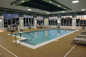 Una amplia piscina interior con agua cristalina, rodeada de tumbonas y una escalera que lleva a un nivel superior.