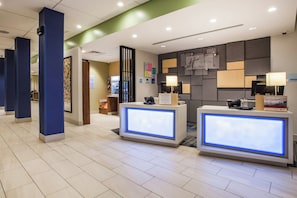 A hotel reception area with a modern design, featuring a reception desk, a refrigerator, and a wall-mounted information board. - Holiday Inn Express & Suites Lexington Park-California by IHG (California)