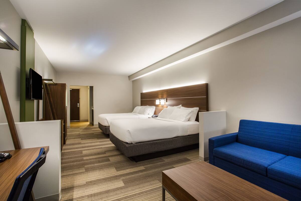 Una habitación de hotel con dos camas, un sofá azul, un escritorio y un televisor.