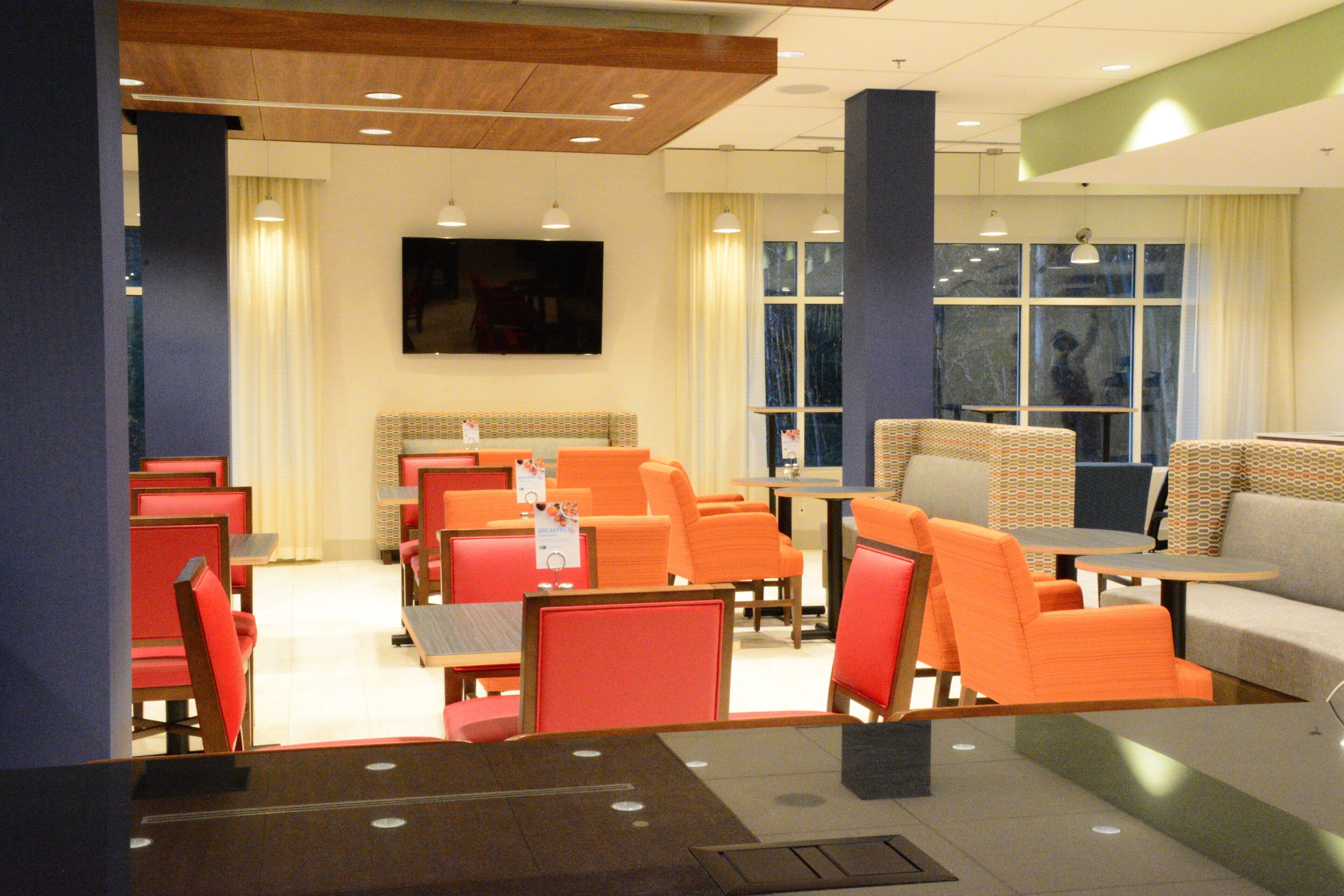 A hotel room with a television, orange and red seating, a large window, and a flat-screen TV mounted on the wall.