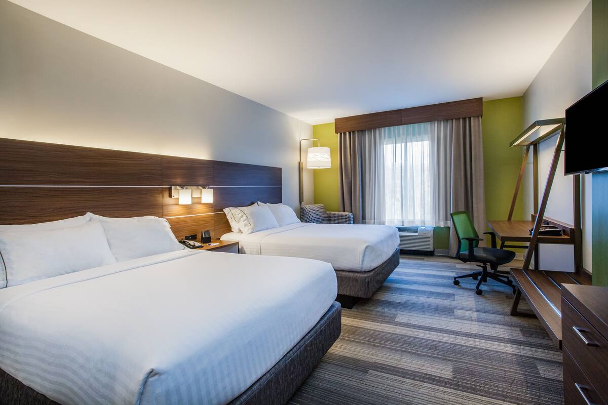 Habitación de hotel con dos camas, un escritorio, una silla, un televisor y una ventana con cortinas.