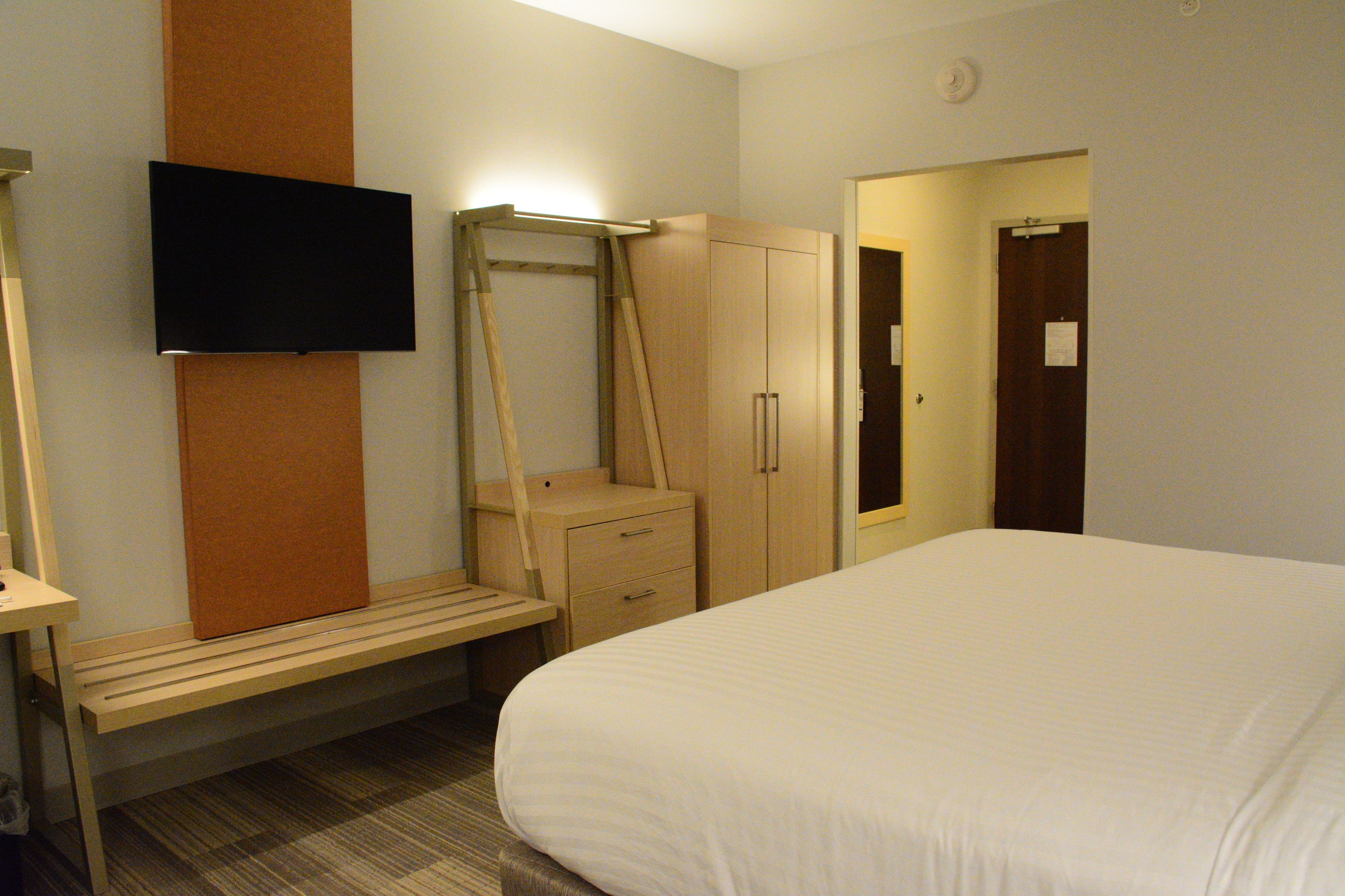 Une chambre d’hôtel équipée d’un lit, d’un bureau, d’une chaise, d’une armoire et d’un téléviseur fixé au mur.