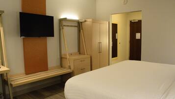 Une chambre d’hôtel équipée d’un lit, d’un bureau, d’une chaise, d’une armoire et d’un téléviseur fixé au mur.