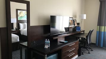 A hotel room with a bed, a desk with a computer, a TV, and a mirror.