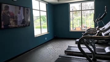 A gym with treadmills, a clock, and large windows.