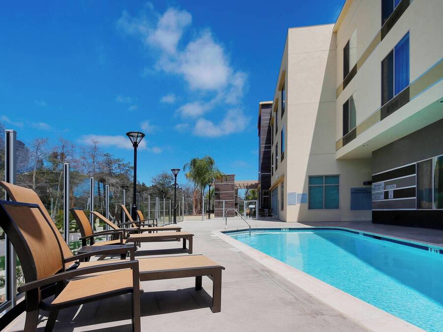 Un espace aménagé au bord de la piscine, avec des chaises longues et une piscine, le tout entouré de bâtiments modernes et sous un ciel dégagé.