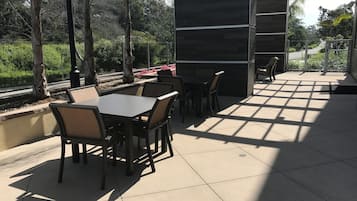 An outdoor patio with tables and chairs, surrounded by trees and a view of a road.