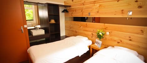 Habitación de hotel con dos camas, cabecero de madera, mesita de noche con un florero, espejo y armario.