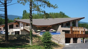 A modern building with a stone facade, a flat roof, and a balcony with umbrellas. - Hôtel le Pré du Lac (Saint-Jorioz)