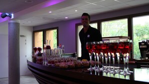 A bar area with a counter, glasses of red wine, and a person standing behind the bar. - Hôtel le Pré du Lac (Saint-Jorioz)