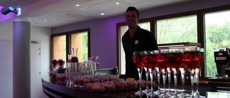 A bar area with a counter, glasses of red wine, and a person standing behind the bar.
