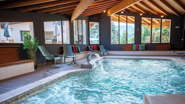 A spa area with a hot tub, seating, and large windows offering views of the outdoors. - Hôtel le Pré du Lac (Saint-Jorioz)