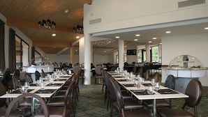 A spacious dining area with long tables set for multiple guests, featuring a high ceiling with wooden beams and recessed lighting. - Hôtel le Pré du Lac (Saint-Jorioz)