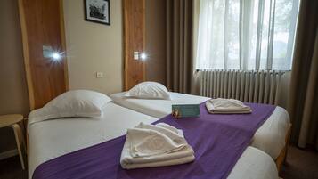 A hotel room with two beds, a purple bedspread, white pillows, and a folded towel on each bed.