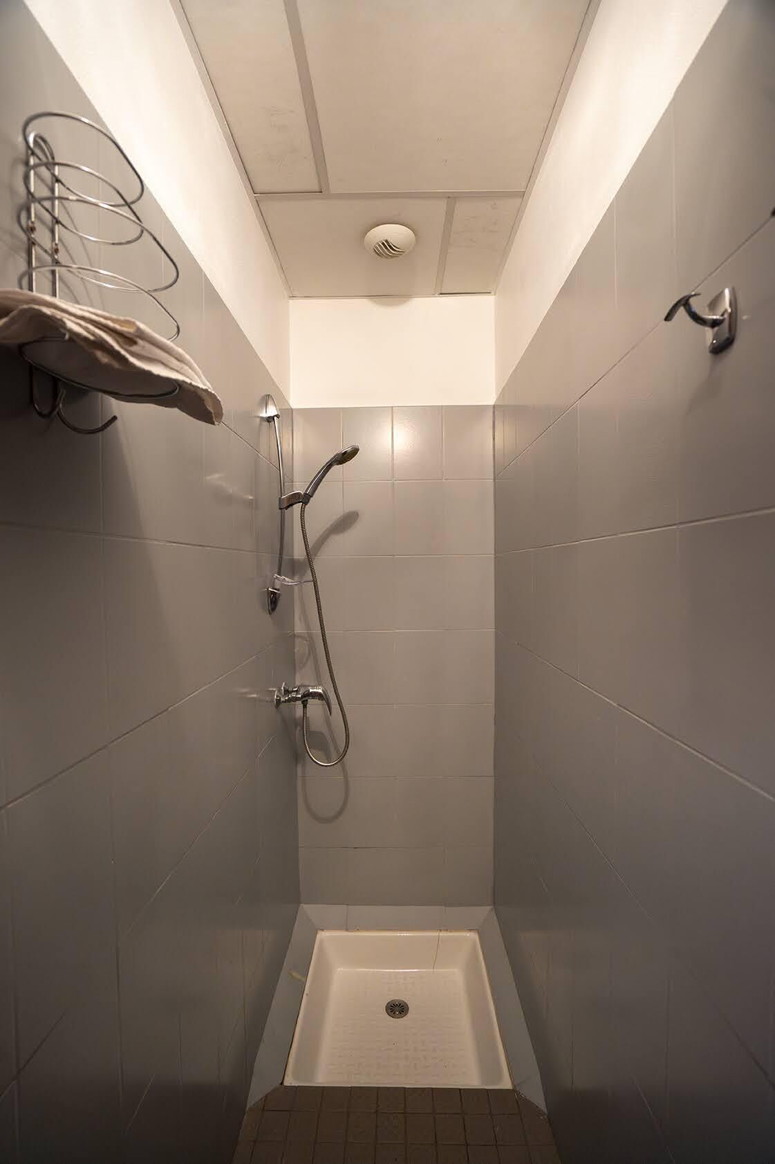 Un pequeño box de ducha con azulejos, un cabezal de ducha manual y un grifo empotrado en la pared.