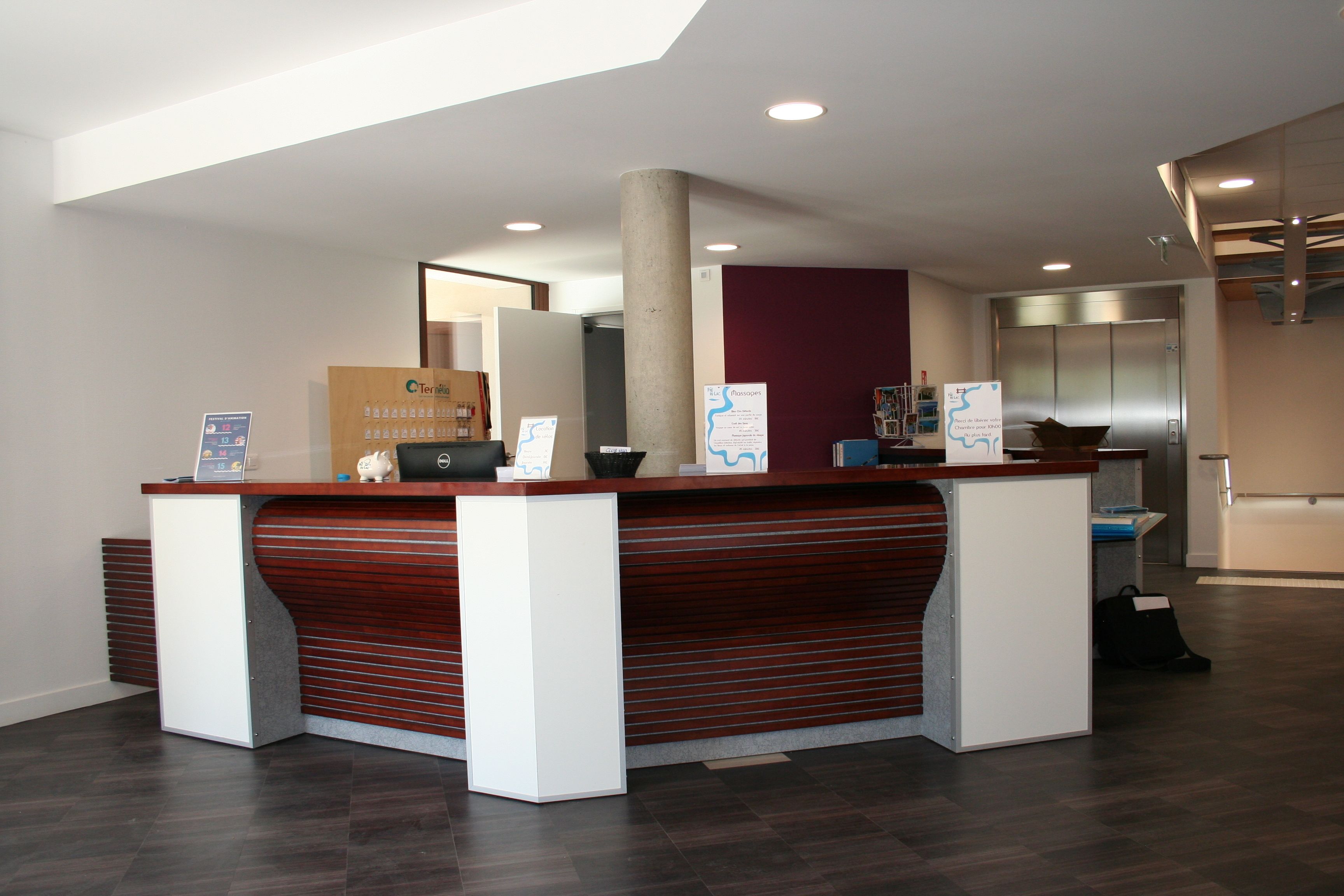 Egy modern dizájnú recepciós pult, egy nagy oszlop és a háttérben egy lift.