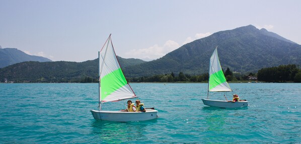 Two sailboats on a calm lake with mountains in the background.