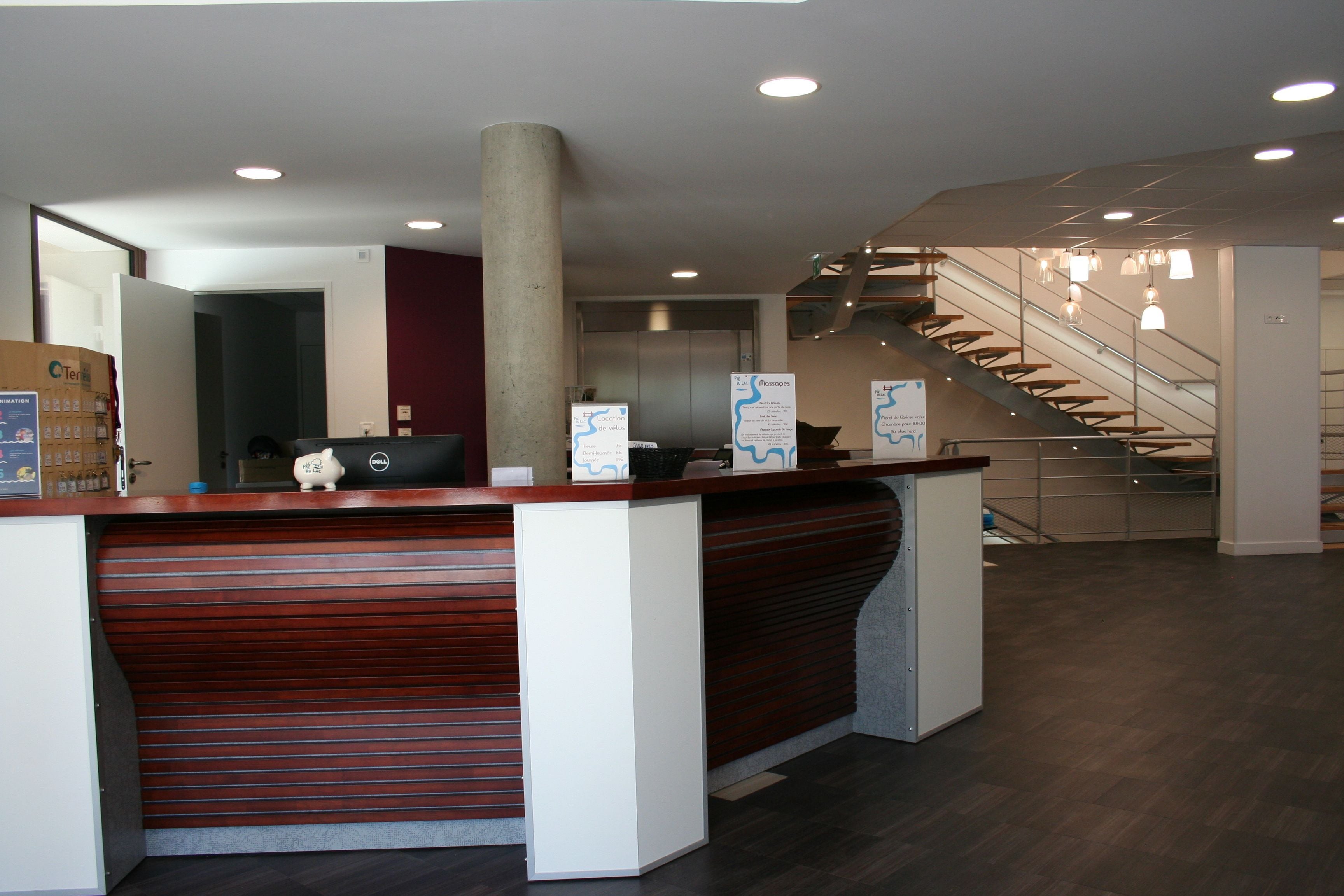 A reception desk with a wooden counter and a white panel, a large pillar, and a staircase with metal railings.