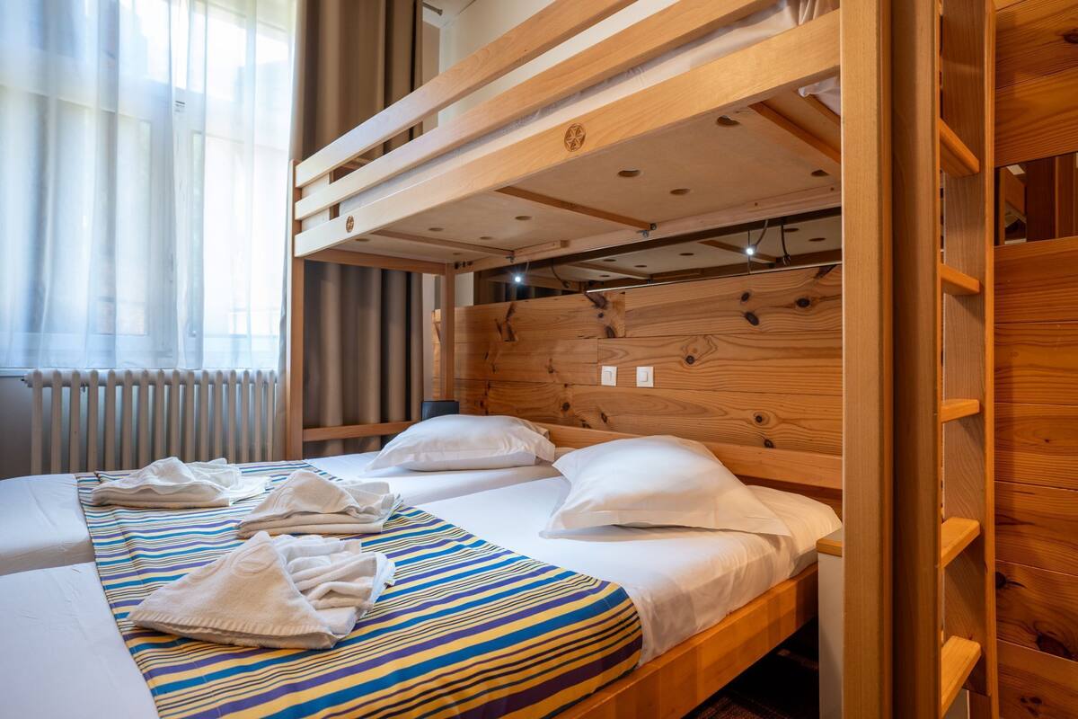 Une chambre avec un lit superposé, une tête de lit en bois, deux lits et une couverture à rayures.