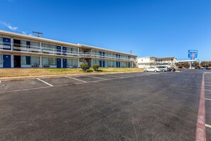 A motel with a parking lot, a sign for The Stockyards, and a clear blue sky. - Bhavani Ma Corp. dba Stockyards Inn & Suites (Fort Worth)