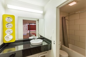 A bathroom with a black countertop, a white sink, a mirror, and a shower area. - Bhavani Ma Corp. dba Stockyards Inn & Suites (Fort Worth)