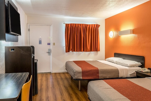 A hotel room with two beds, a desk, a chair, a TV, and a bathroom door.