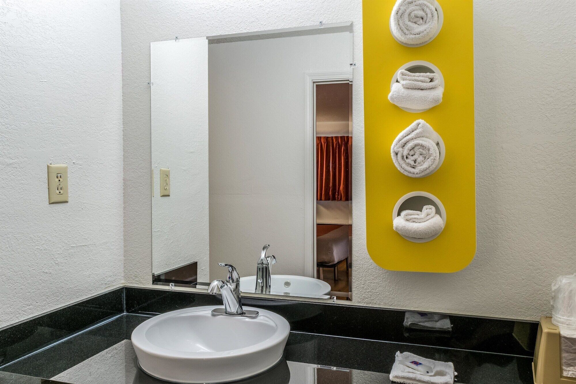 A bathroom with a white sink, a mirror, and a yellow towel rack with towels.