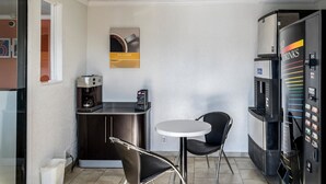 Un petit café avec une machine à café, une seule table avec une chaise et un distributeur automatique.