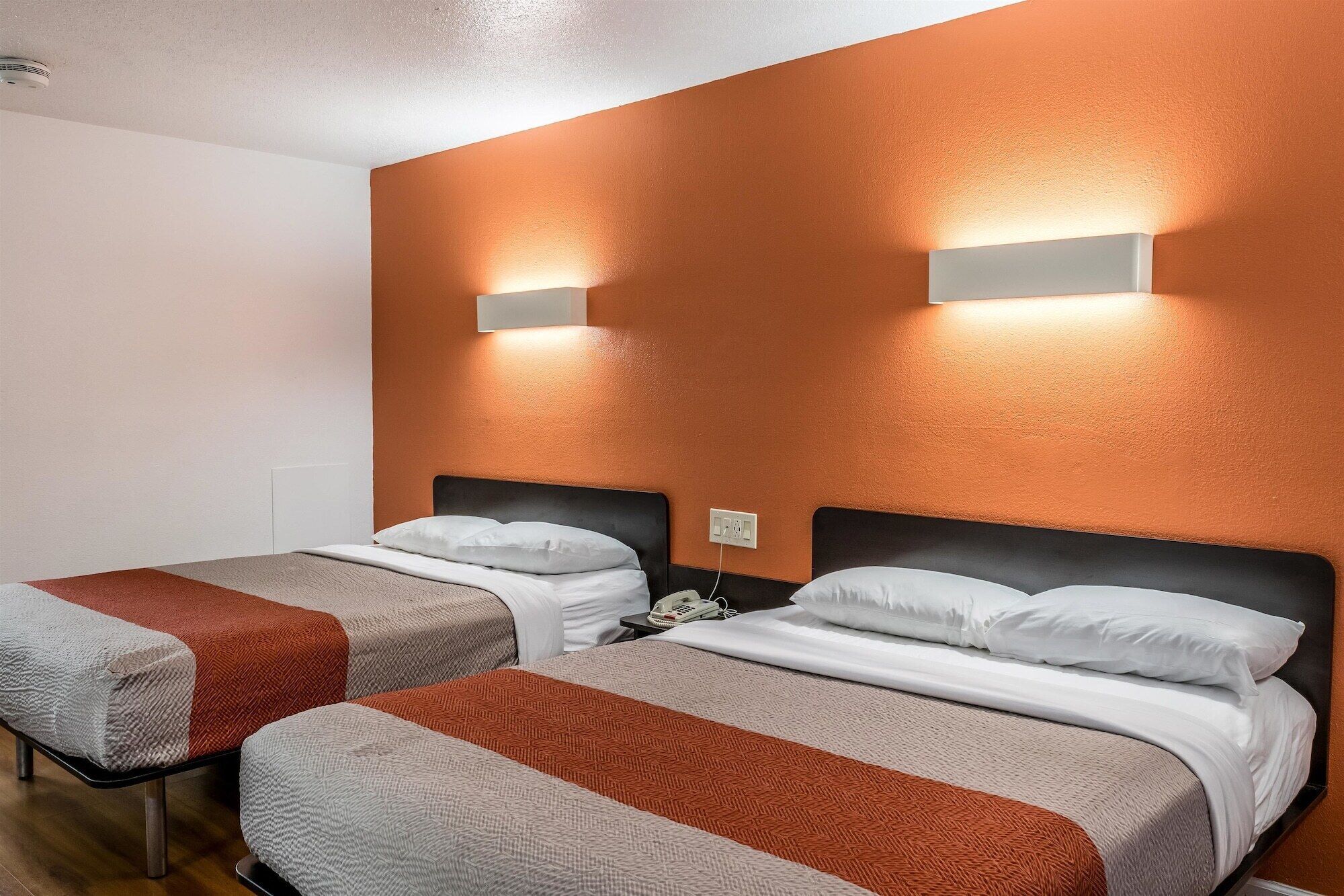 A hotel room with two beds, each with a headboard, a bedside table, and a telephone.