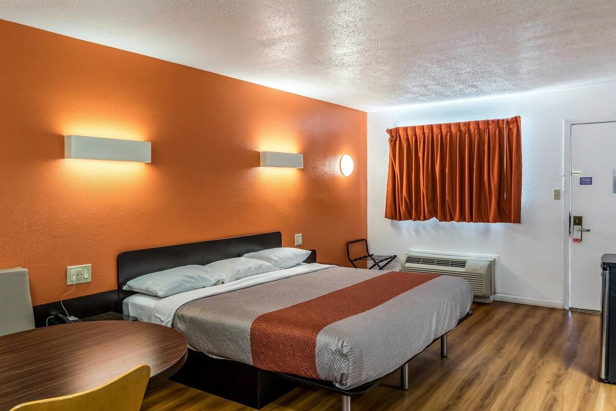 Une chambre d’hôtel équipée d’un lit, d’un bureau, d’une chaise, d’un appareil de climatisation et d’une fenêtre avec des rideaux.