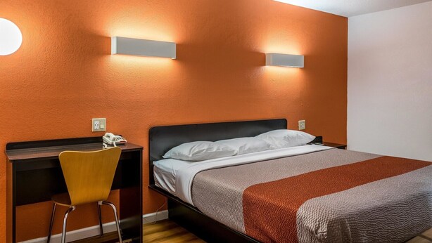 Une chambre d’hôtel comprenant un lit, un bureau avec une chaise et deux lampes fixées au mur.