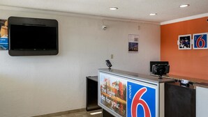 Un espace d’accueil de motel avec un téléviseur à écran plat fixé au mur, un panneau d’affichage présentant une image attrayante et un texte, ainsi qu’un panneau indiquant le chiffre « 6 », qui représente le nom du motel.