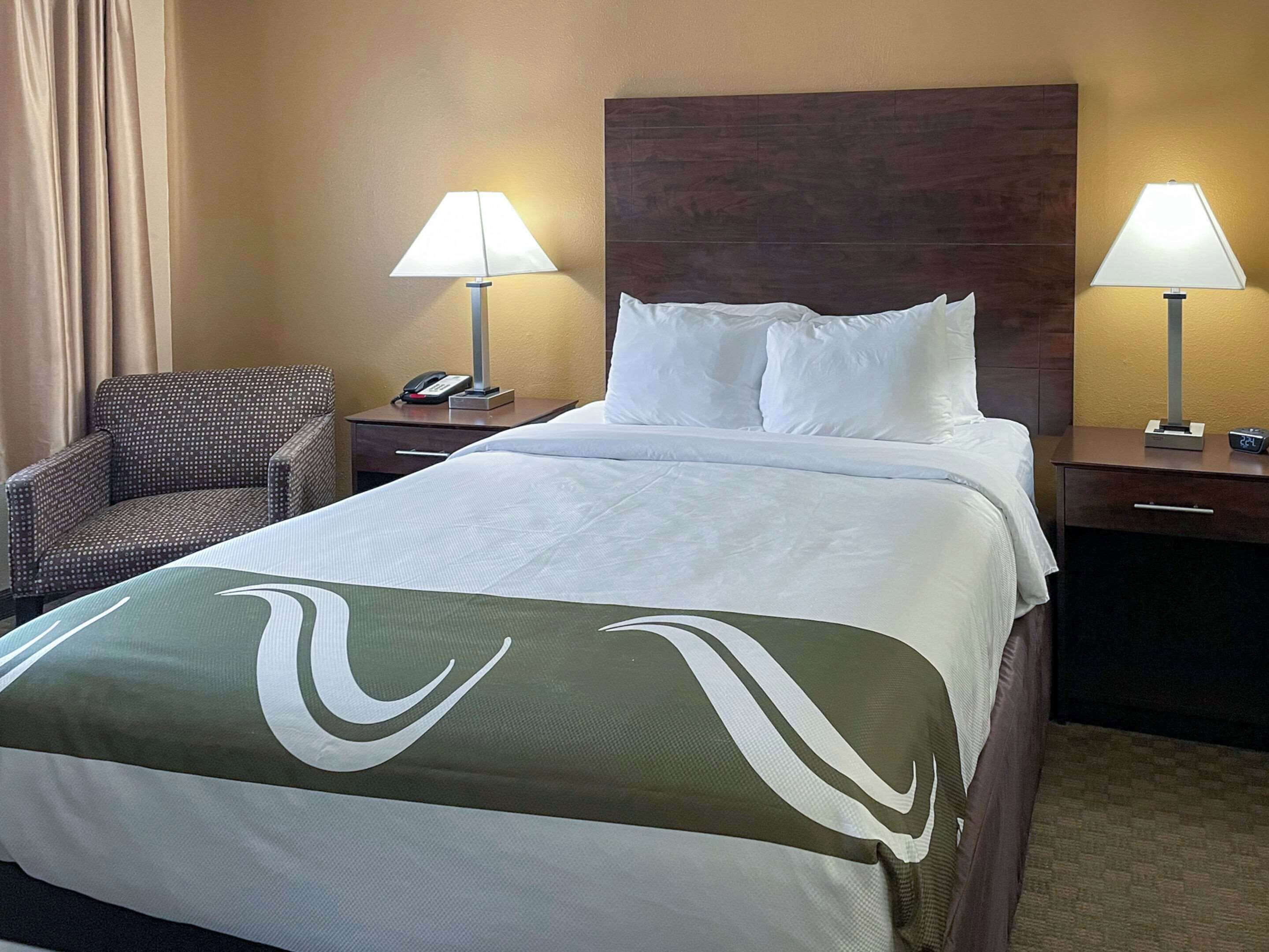 A hotel room with a large bed, two bedside tables, a chair, and a lamp on each side.