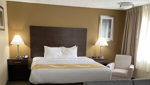 Ein Hotelzimmer mit einem großen Bett, zwei Nachttischen mit Lampen, einem grauen Sessel und einem Kopfteil.
