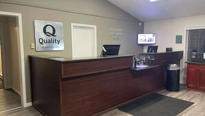 Ein Hotelrezeptionstresen mit einem Schild, das "Quality by Choice Hotels" zeigt, einem Fernsehbildschirm und einem Papierkorb.