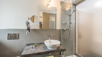 Une salle de bain moderne avec un grand miroir, un lavabo blanc et une douche à parois de verre.