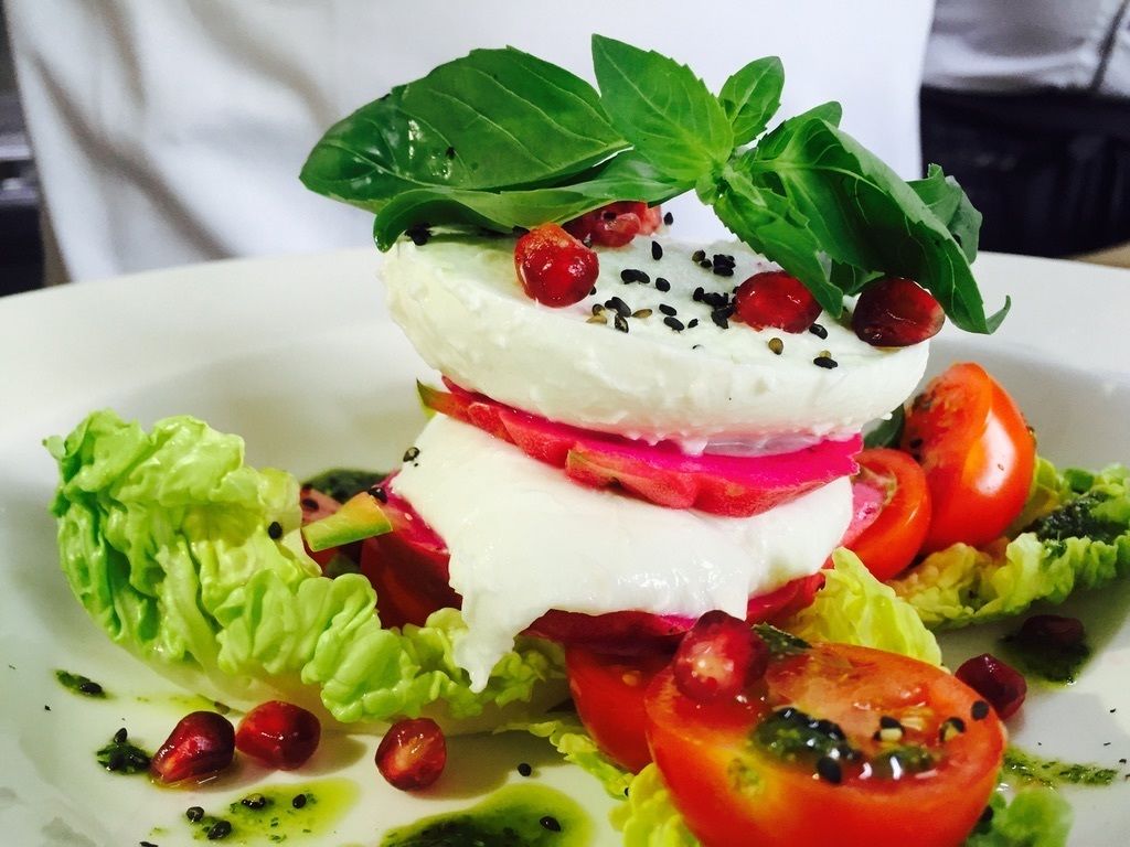 A layered salad with tomatoes, lettuce, and a basil leaf on a white plate.